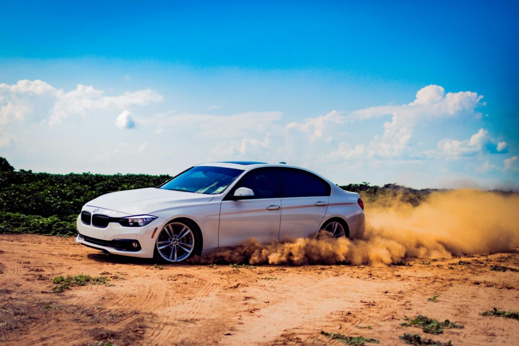 Confident East London learner driving a white sports car in a desert-like area with dust swirling around.